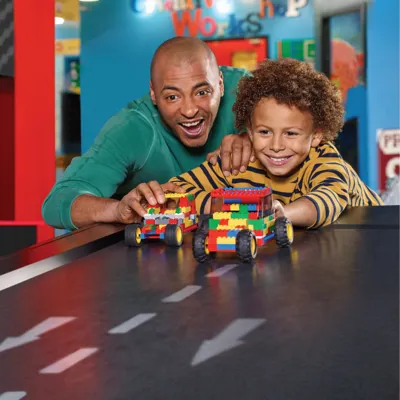 Excited boy and man racing colorful LEGO cars down a fun ramp at LEGOLAND Discovery Center Michigan, showcasing a vibrant play area filled with creativity and teamwork