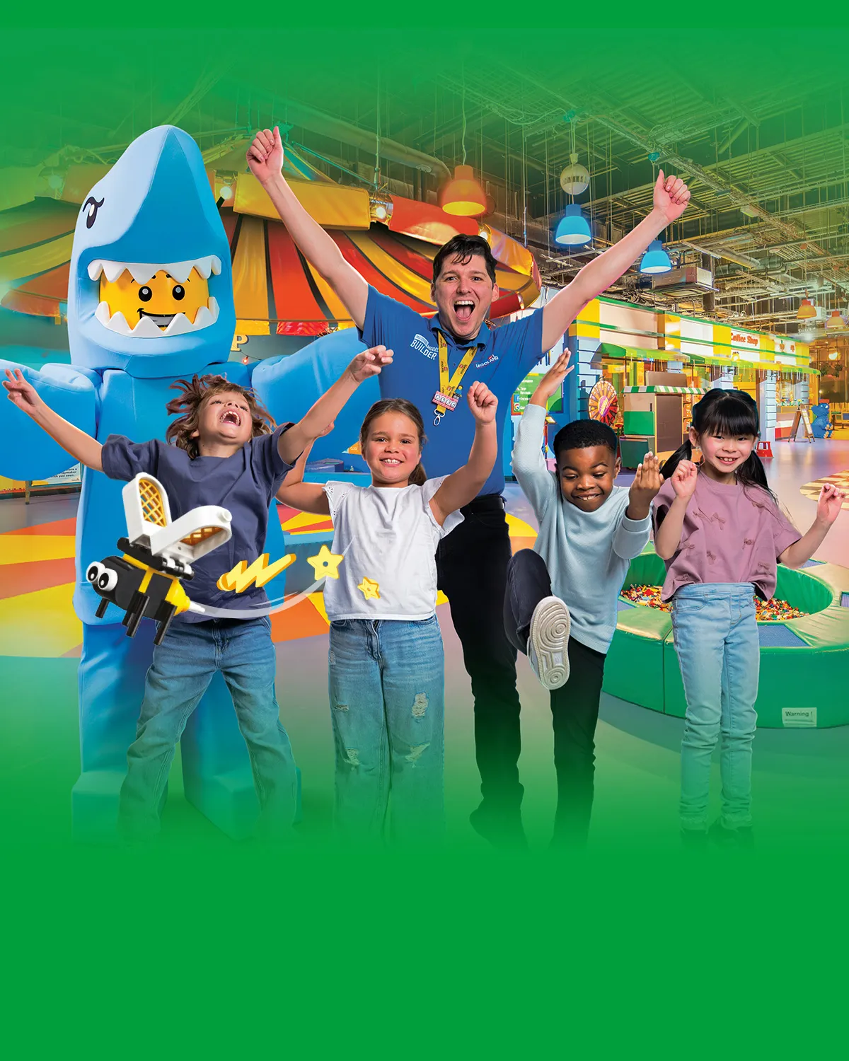 Kids and a LEGOLAND staff member celebrate with a LEGO shark character in a colorful indoor play area.
