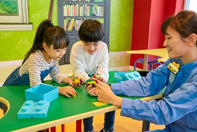 alt="「マスタービルダーアカデミー」でレゴ職人のマスター・ビルダーと一緒にレゴビルドを楽しむ男の子と女の子"